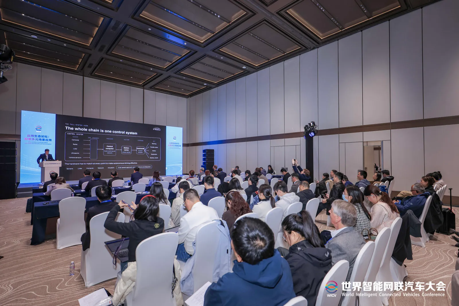 Delegates in the forum hall, some raising phones to photograph the slide The whole chain is one control system.
