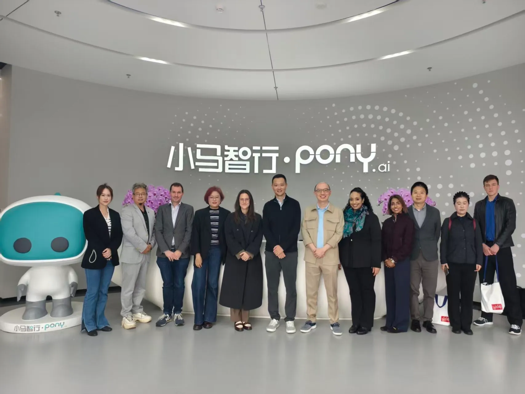 The delegation with Pony.ai hosts in the reception area at Pony.ai in Beijing, beside the company logo and its robot mascot.